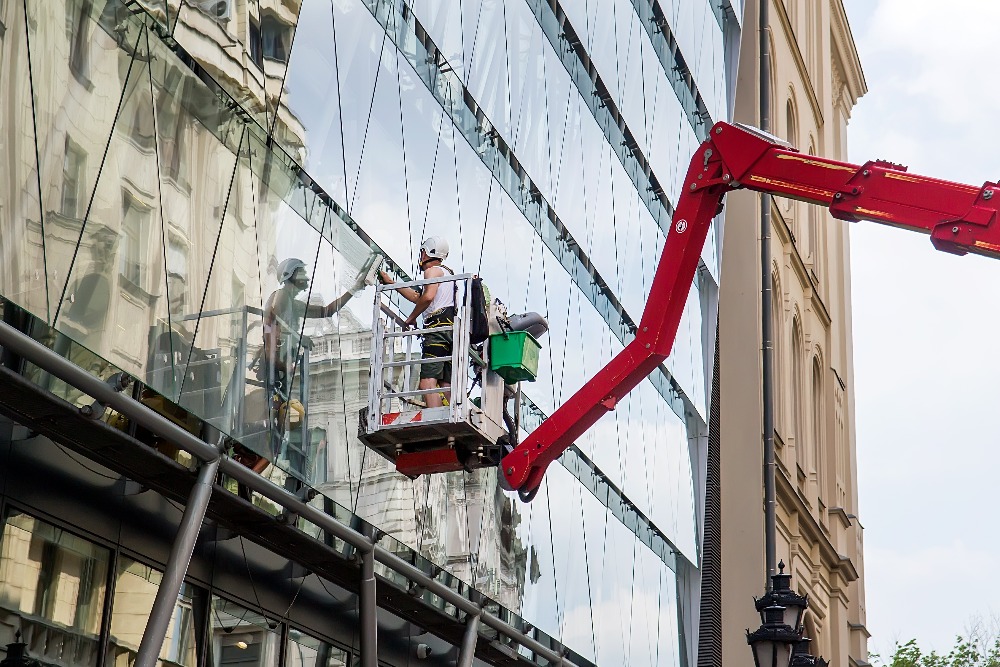 Worker in elevated work platform cleaning building facade window glass by using equipment tools to cleanup dirty surface selective focus jpg